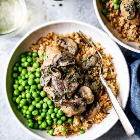 Braised chicken in a creamy mushroom sauce served over rice with a side of bright green peas.
