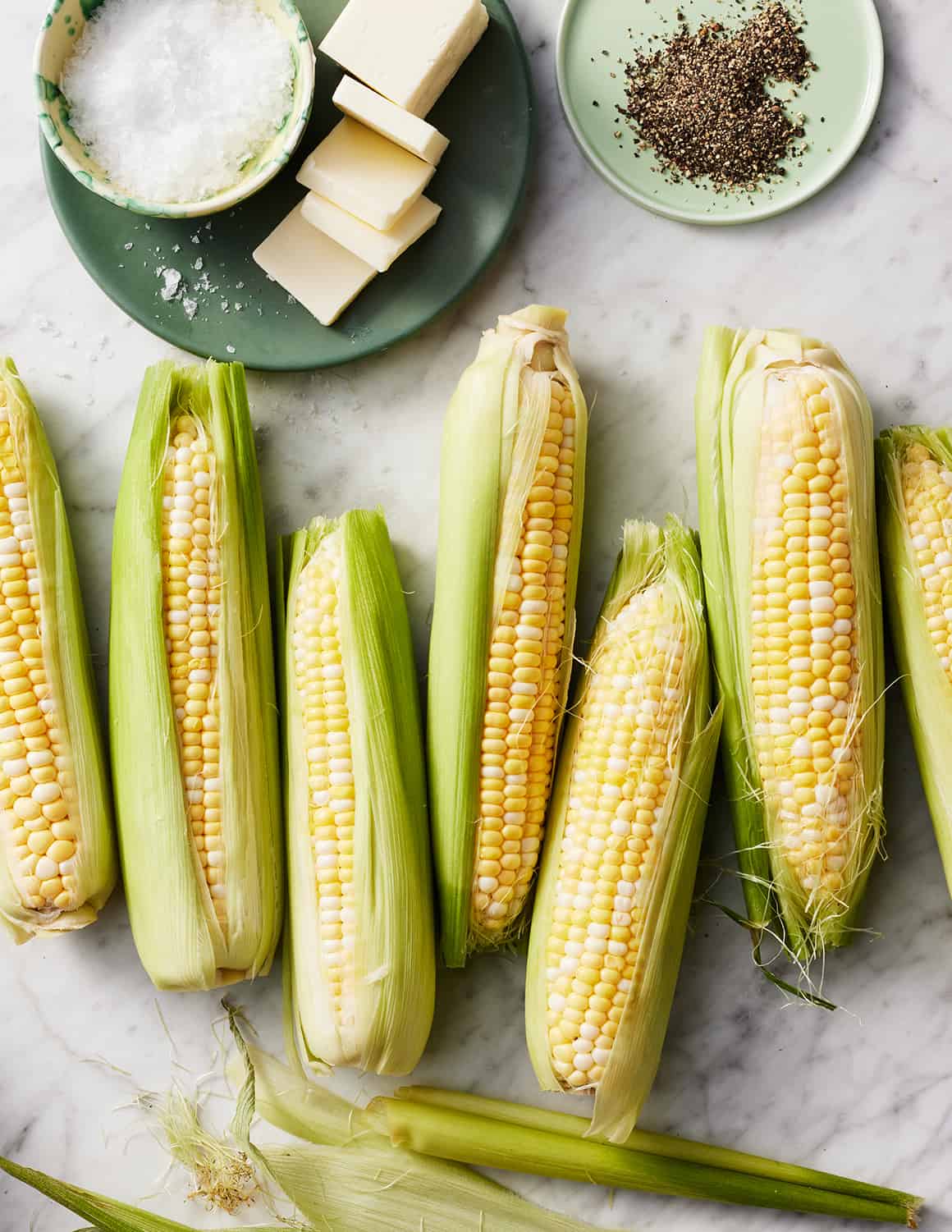 Fresh sweet corn next to butter, salt, and pepper