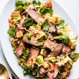 Sliced medium-rare steak over a bed of greens and noodles, a vibrant and easy meal to cook for a date.